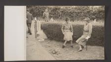 [Two women on a lawn seated on stick chairs, a British Army Corporal stands nearby ]
