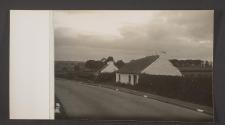 [Whited washed stone buildings with thatched roofs at edge of motorway]