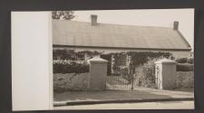 [A man stands in front of a white stone house]