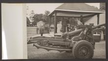 [King George VI, Queen Elizabeth and assorted British Army generals standing on a reviewing platform, as artillery is towed past.]