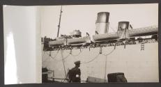 [Troop shipping pulling away from a quay, its railings are lined with people.]