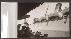 [Troop shipping pulling away from a quay, its railings are lined with people.]