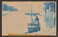 [Young man with cooking equipment in small boat with awning]