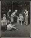 [Young man photographing a family as they prepare food on the grill in the backyard]