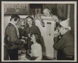[A teenage boy taking pictures of his friends gathered around an open refrigerator after being outside in the winter]