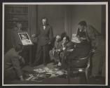 [A group of Kodak executives in an office view advertising layouts displayed on an illuminated viewing machine]