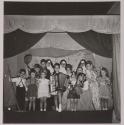 [Rosa Maria Toscano (center right), child of the photographer, on stage with other children during a performance]