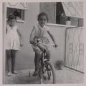 [Rosa Maria Toscano (center), child of the photographer, playing on a bicycle with a friend]
