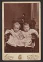 [Two infants, seated in chair]