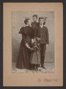 [Group portrait with young boy measuring two older children]