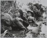 [Vietnamese women and children crouching in a water filled ditch]
