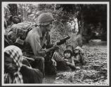 Bao Trai, Vietnam 1966 - Vietnamese children gaze at an American paratrooper holding an M79 grenade launcher, as they cling to their mothers