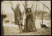 [Two women with cloaks and walking sticks standing in front of trees, members of the Suffrage Hike]