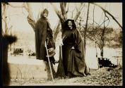 [Two women with cloaks and walking sticks standing in front of trees, members of the Suffrage Hike]
