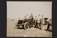 [Automobile with driver and passenger, three men standing alongside]
