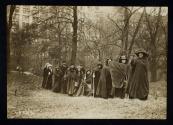 [Group of eleven women standing with cloaks, walking sticks and a banner that reads "Votes For Women Pilgrimage from New York City to Washington, DC 1913", three men standing in background]