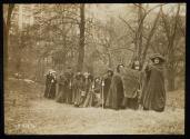 [Group of eleven women standing with cloaks, walking sticks and a banner that reads "Votes For Women Pilgrimage from New York City to Washington, DC 1913", three men standing in background]