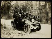 [Group of eleven women, three men and one small girl piled onto an automobile with signs advocating Votes for Women]