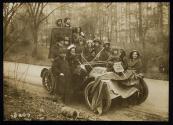 [Group of eleven women, three men and one small girl piled onto an automobile with signs advocating Votes for Women]