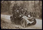 [Group of eleven women, three men and one small girl piled onto an automobile with signs advocating Votes for Women]
