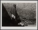[Sideview of a woman in shawl standing against a wall with a shadow]