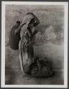 [Girl standing next to wall with pottery vessel on her back]