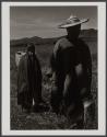 [Man with hat and boy in field wearing ponchos]