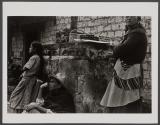 [Three people against wall, one sitting wearing hat]