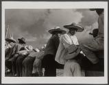 [Group of men, some leaning over fence, all wearing hats]