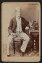 [Man seated at a table, cat and beverage atop]