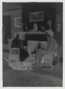 [John Spargo seated near fireplace with woman and dog]