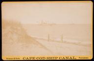 [Two men on beach with boats in background]