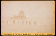 [Group on shore with bucket dredge in background]