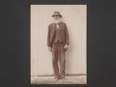 [Old man standing beside a building]