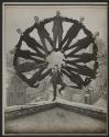 [Man posed on the corner of a rooftop with an arc of eleven suited men balanced on his shoulders]