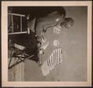 [Man seated at a small table reading a newspaper]